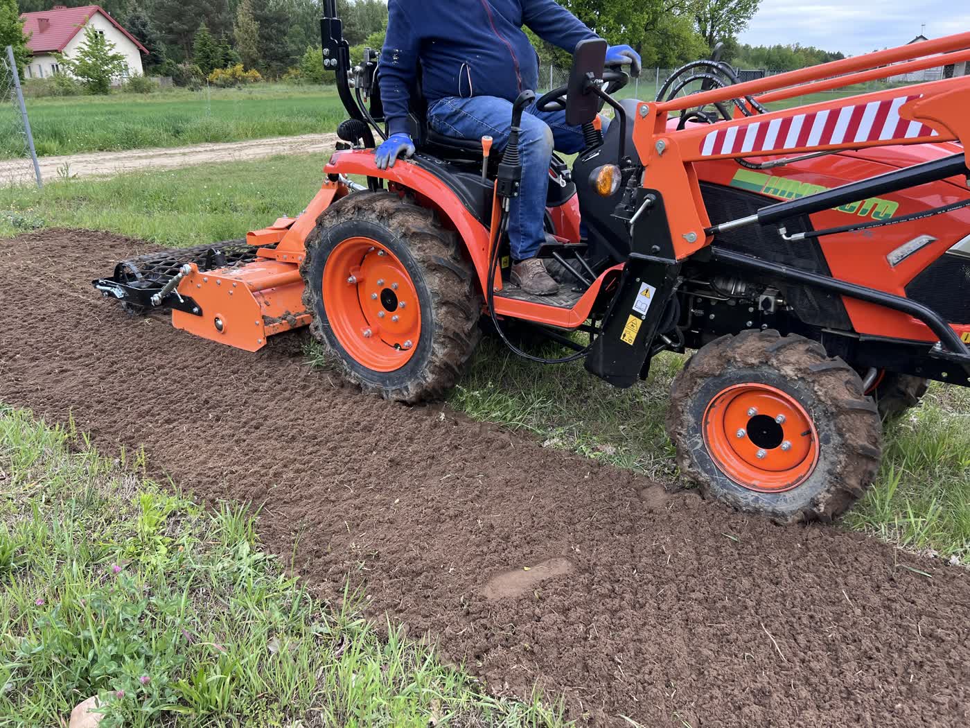 Mini traktor z glebogryzarką separacyjną przygotowuje pas ziemi pod trawnik